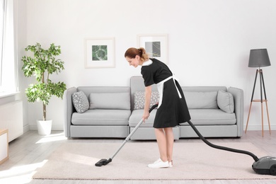 Photo of Female worker removing dirt from carpet with professional vacuum cleaner indoors