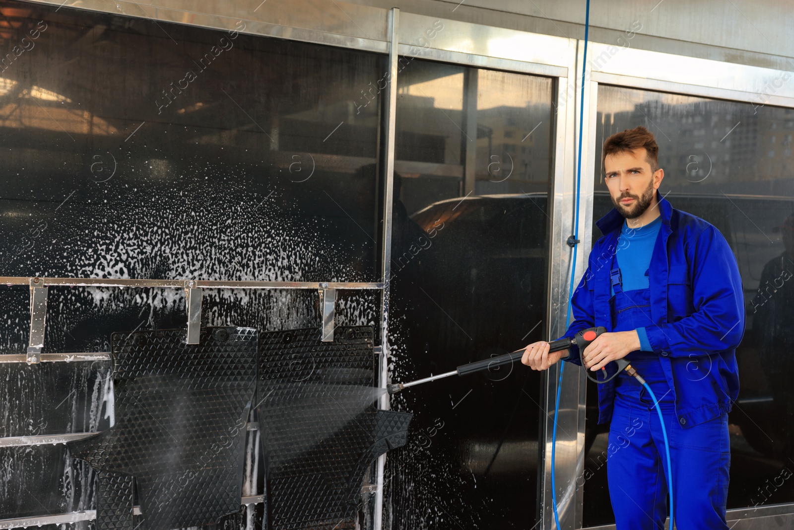 Photo of Worker cleaning auto mats with high pressure water jet at car wash