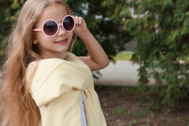 Photo of Girl in stylish sunglasses near spruce trees outdoors. Space for text