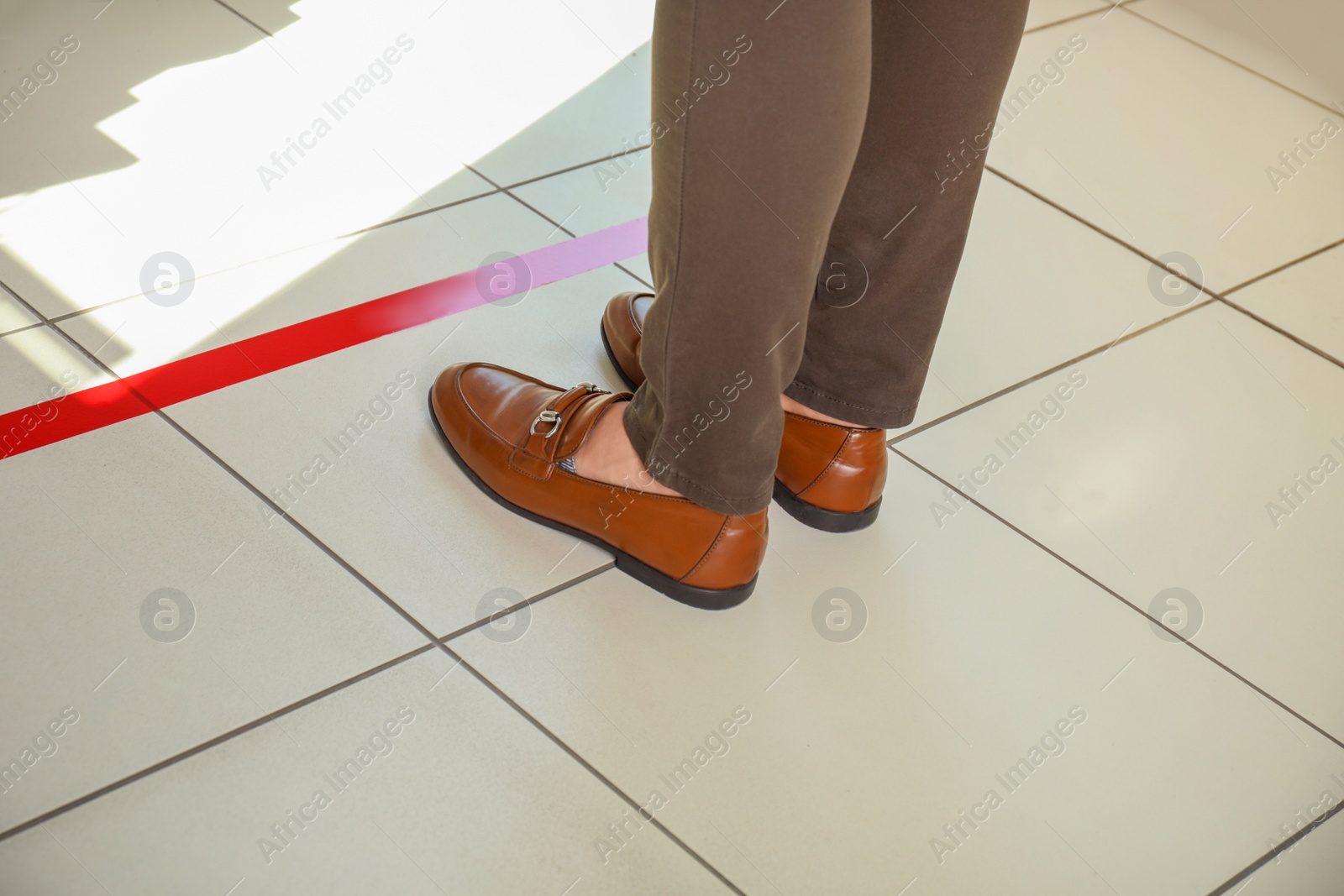 Photo of Man standing behind taped floor marking for social distance, closeup. Coronavirus pandemic