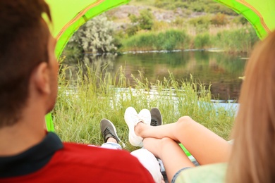 Photo of Young couple resting in camping tent near pond, view from inside