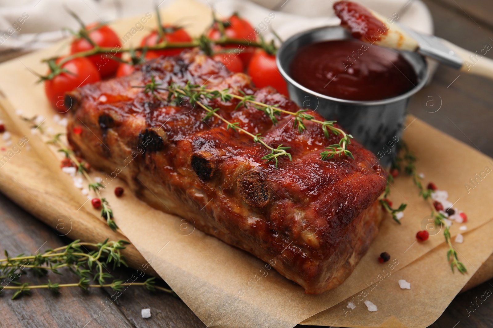 Photo of Tasty roasted pork ribs served with thyme, sauce and tomatoes on wooden table, closeup