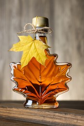 Photo of Leaf shaped bottle of tasty maple syrup on wooden table