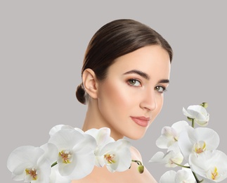 Image of Beautiful young woman and orchid flowers on light background. Spa portrait