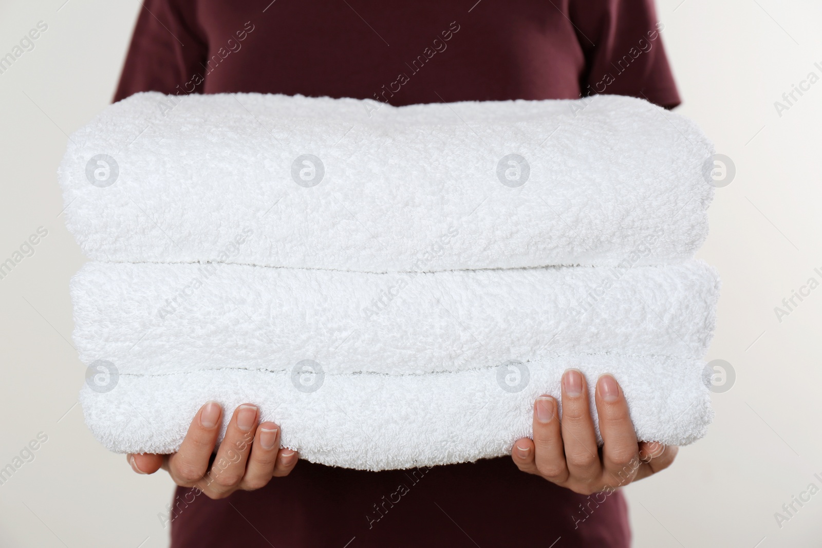 Photo of Woman holding fresh towels on light background, closeup