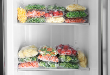 Plastic bags with different frozen vegetables in refrigerator