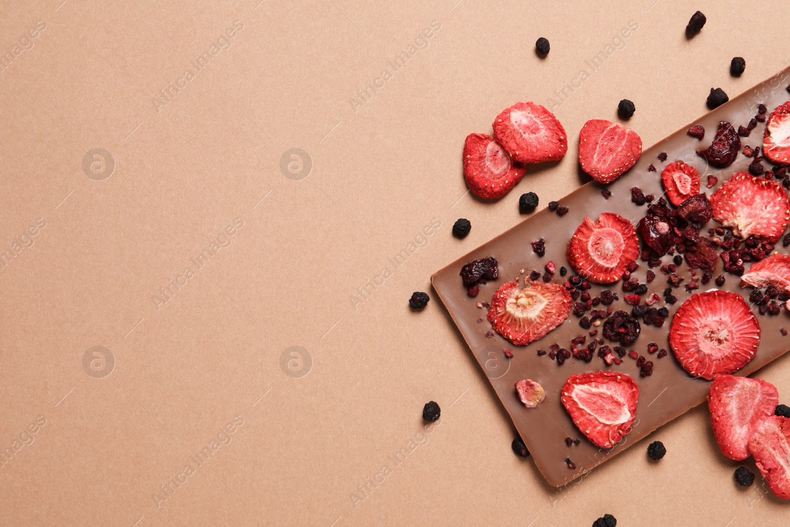 Photo of Chocolate bar with freeze dried fruits on beige background, top view. Space for text