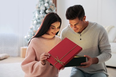 Photo of Couple opening gift box in room with Christmas tree