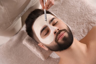 Photo of Cosmetologist applying mask on man's face in spa salon, above view