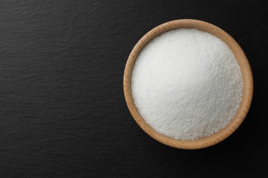 Photo of Granulated sugar in bowl on black table, top view. Space for text