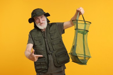 Photo of Fisherman holding fishing net with catch and pointing on yellow background