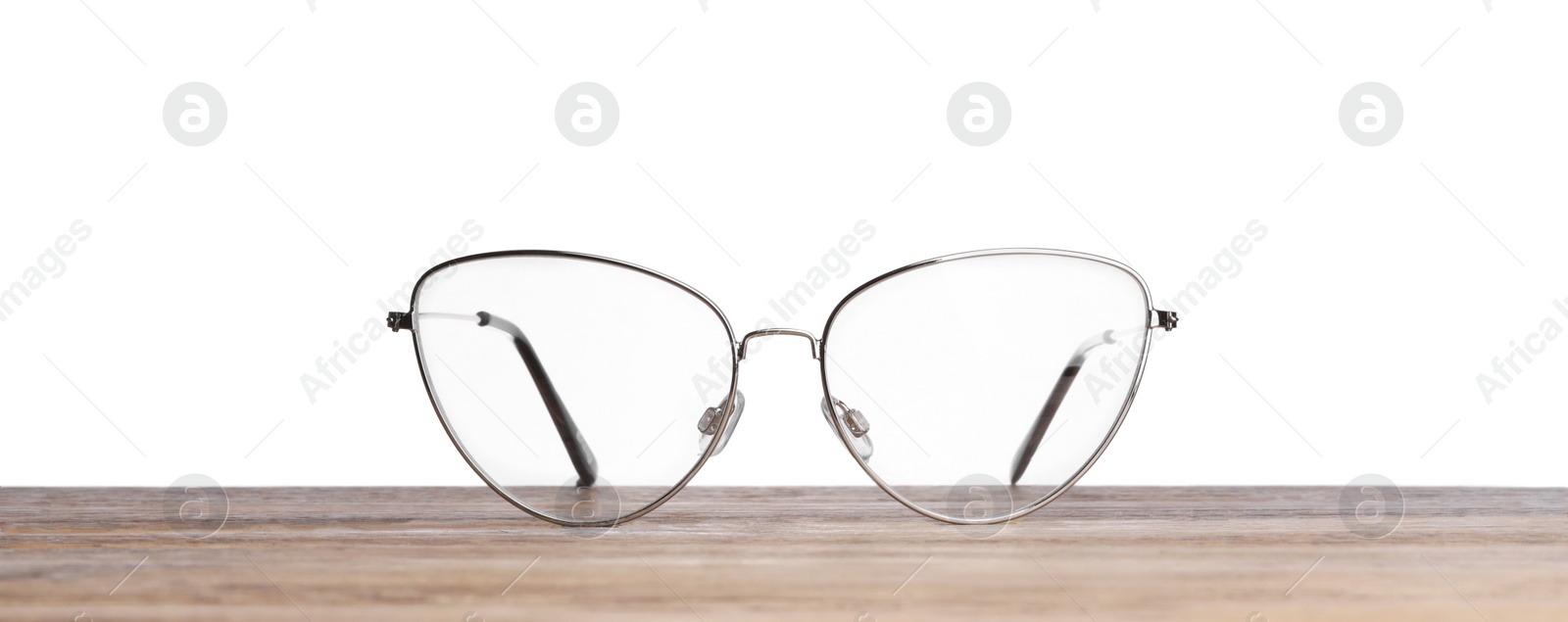 Photo of Stylish glasses with metal frame on wooden table against white background