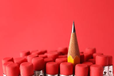 Sharp graphite pencil among others with erasers on red background, closeup. Space for text