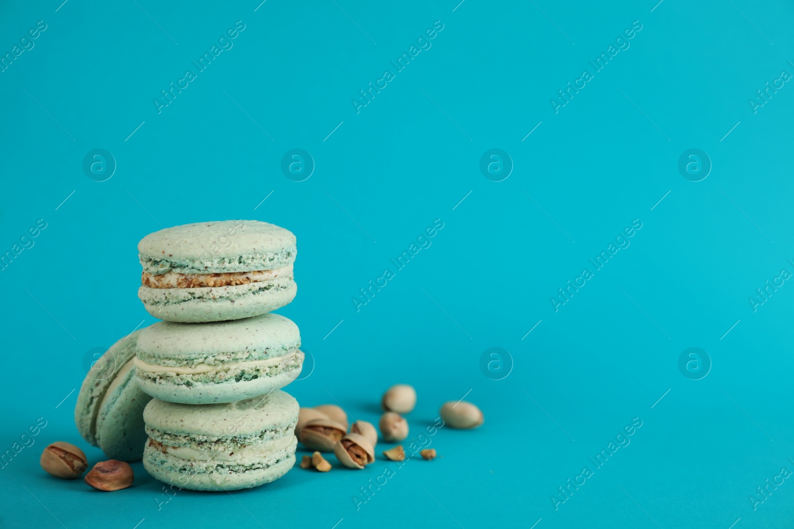 Photo of Delicious macarons and pistachios on light blue background, space for text