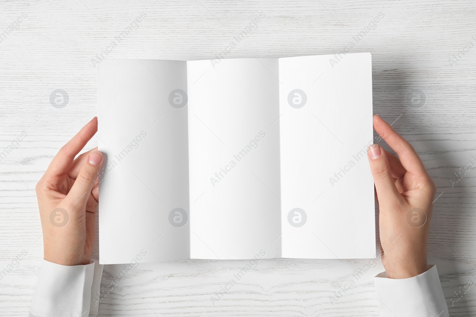 Photo of Woman holding blank brochure mock up on light background, top view