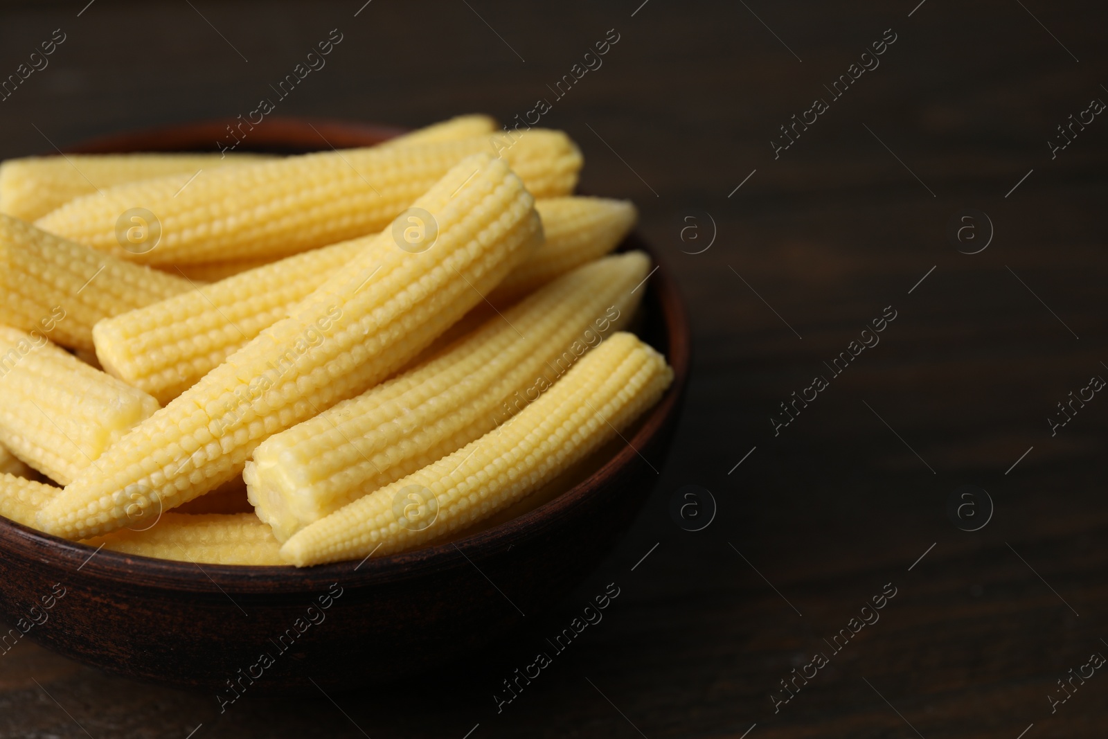 Photo of Tasty fresh yellow baby corns in bowl on wooden table, closeup. Space for text