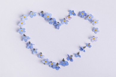 Heart made with beautiful forget-me-not flowers on white background, top view. Space for text