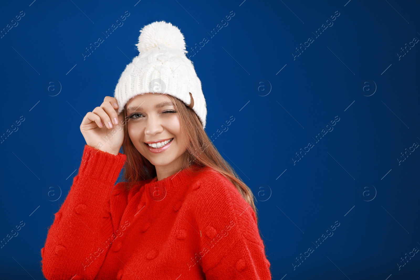 Photo of Young woman in warm sweater and hat on blue background, space for text. Winter season