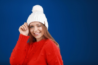 Young woman in warm sweater and hat on blue background, space for text. Winter season