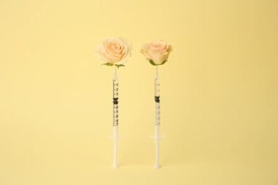 Photo of Medical syringes and rose flowers on pale yellow background