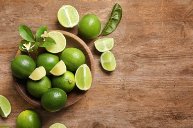 Bowl with fresh ripe limes on wooden background, top view