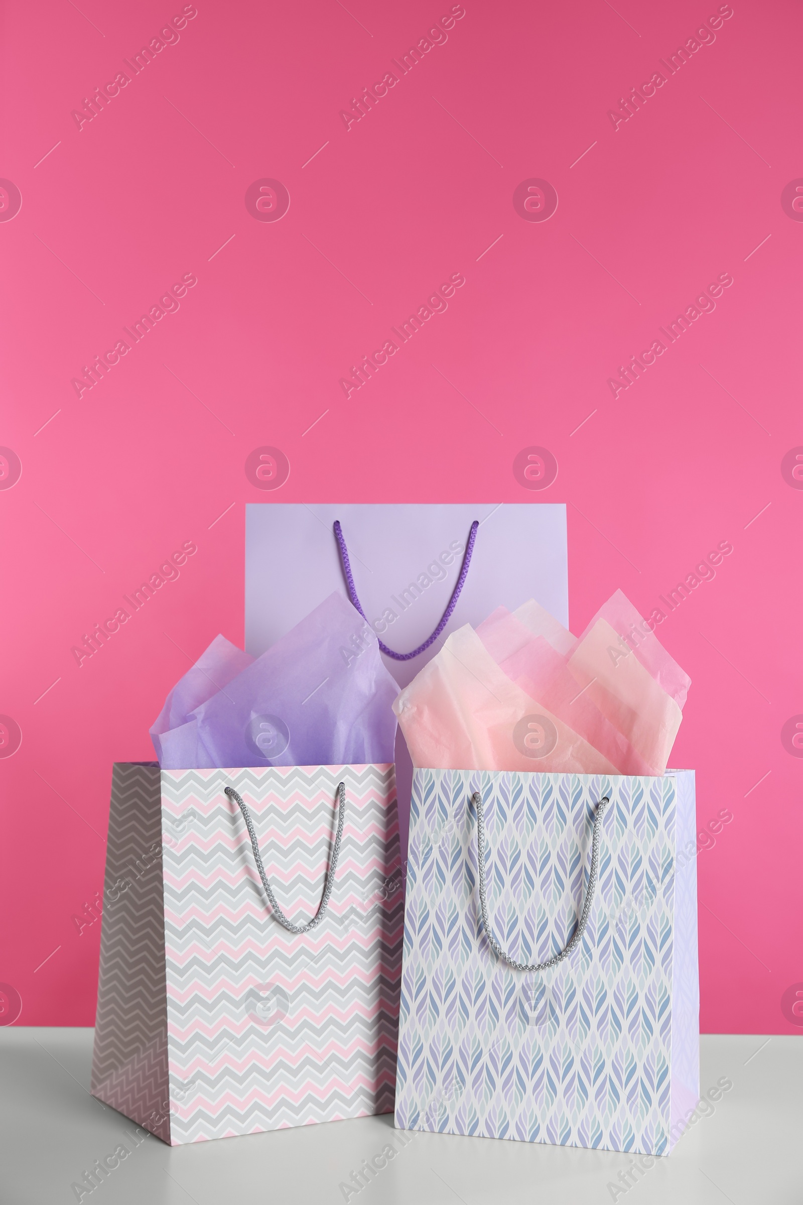 Photo of Gift bags with paper on white table against pink background