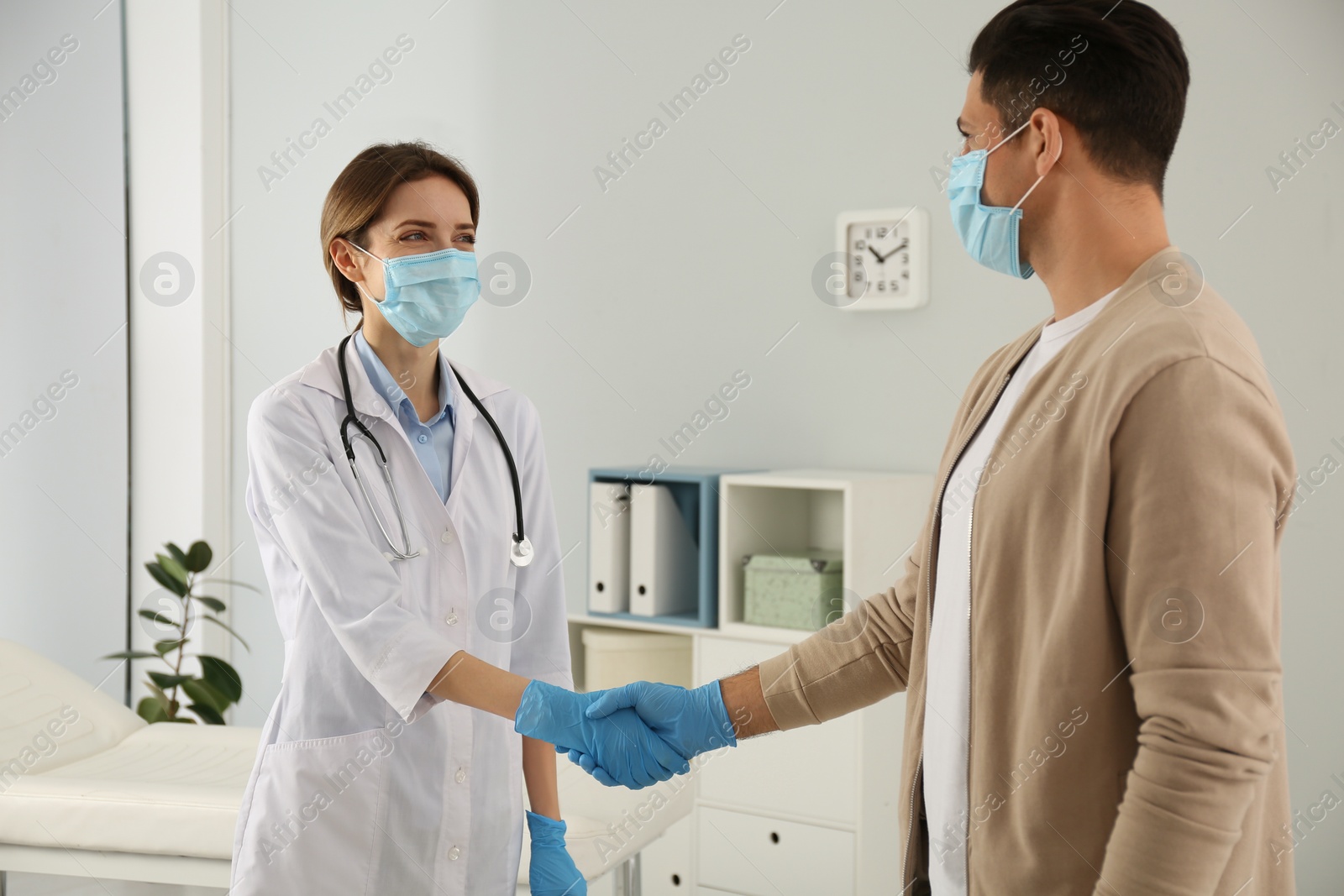 Photo of Doctor and patient in protective masks shaking hands indoors