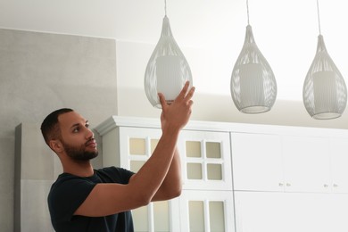 Photo of Young man repairing ceiling lamp indoors, space for text