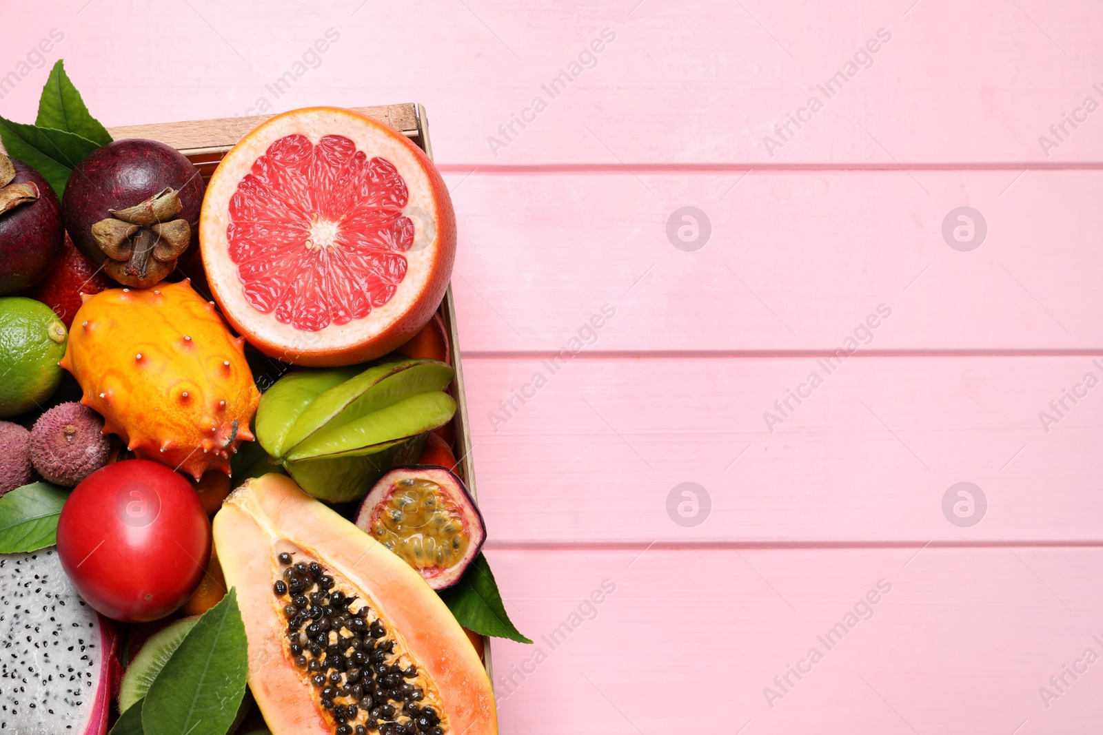 Photo of Different tropical fruits in box on pink wooden background, top view. Space for text