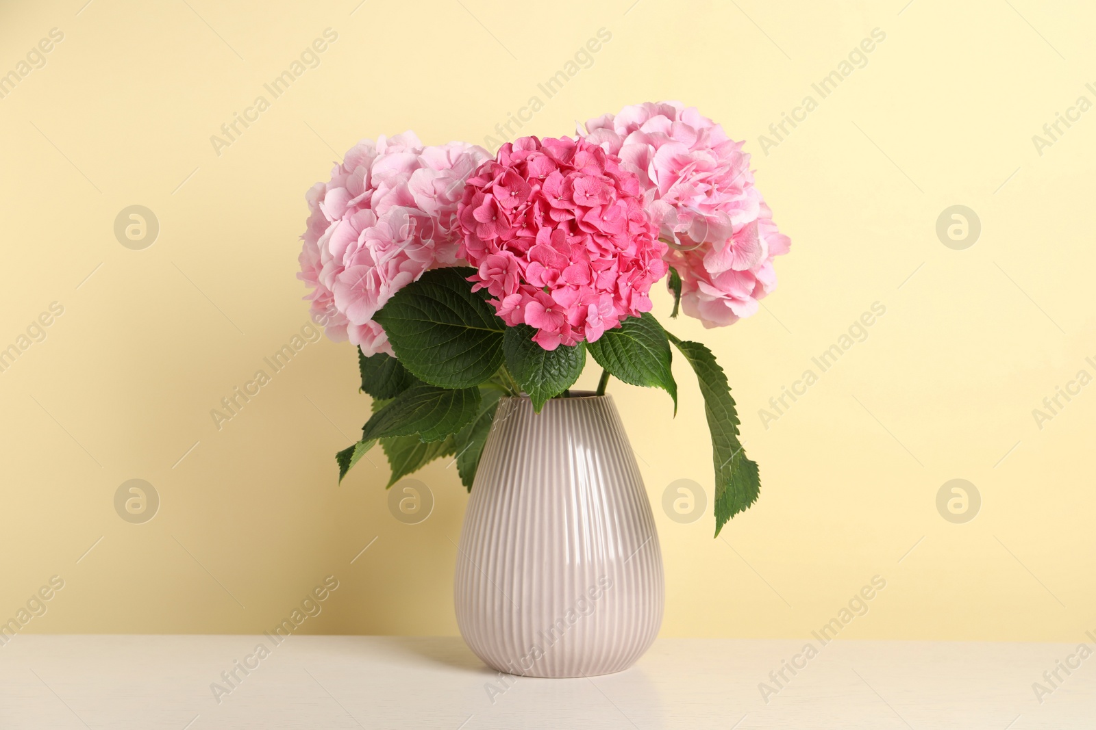 Photo of Bouquet with beautiful hortensia flowers on white wooden table against yellow background