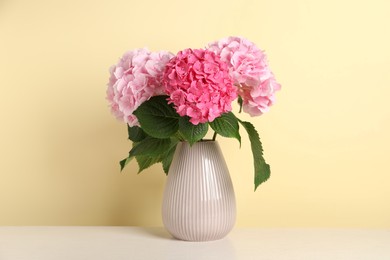 Bouquet with beautiful hortensia flowers on white wooden table against yellow background