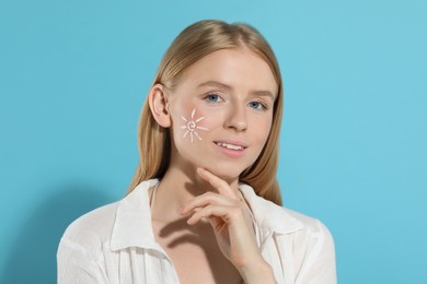 Photo of Beautiful young woman with sun protection cream on her face against light blue background