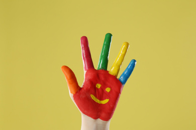 Kid with smiling face drawn on palm against yellow background, closeup