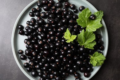 Photo of Plate with ripe blackcurrants and leaves on grey background, top view