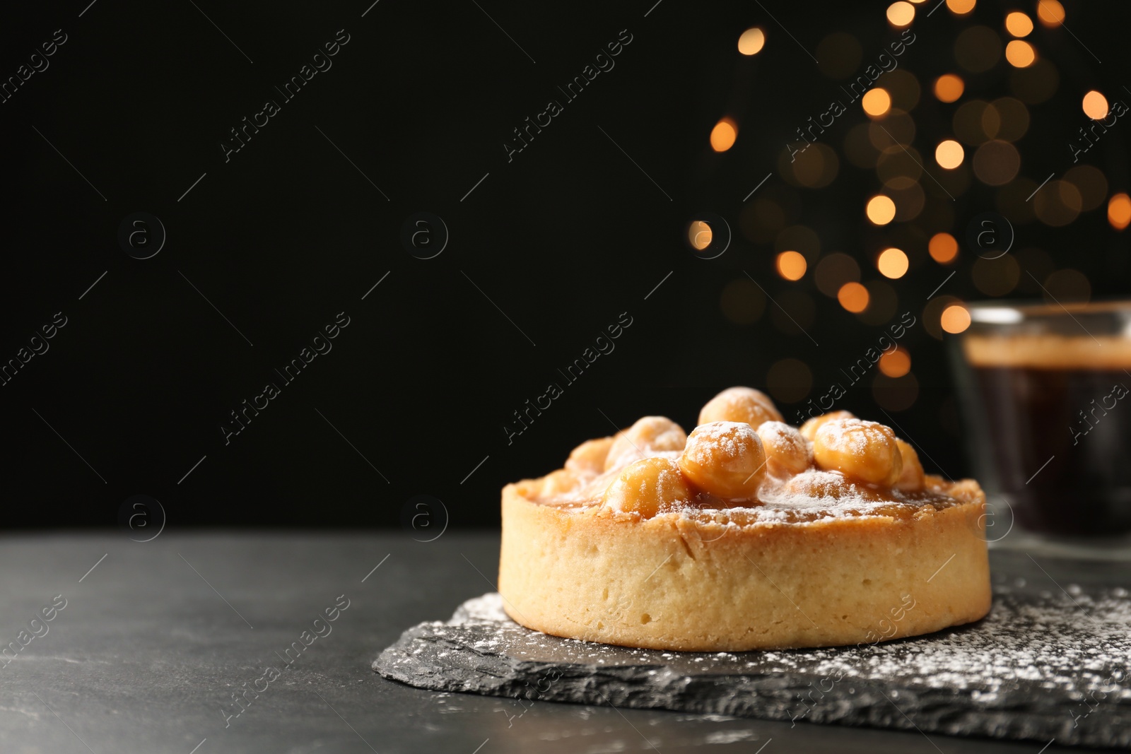 Photo of Delicious tart with hazelnuts, sweet caramel and powdered sugar on black table. Space for text