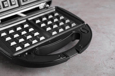 Photo of Modern waffle iron on grey stone table, closeup