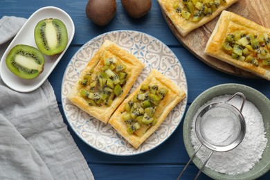 Photo of Fresh tasty puff pastry with kiwi served on blue wooden table, flat lay