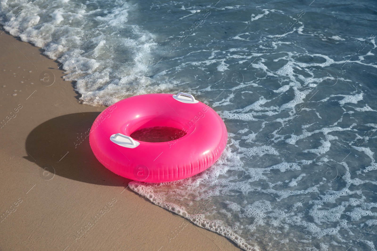 Photo of Bright pink inflatable ring on sandy beach near sea