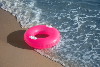 Photo of Bright pink inflatable ring on sandy beach near sea