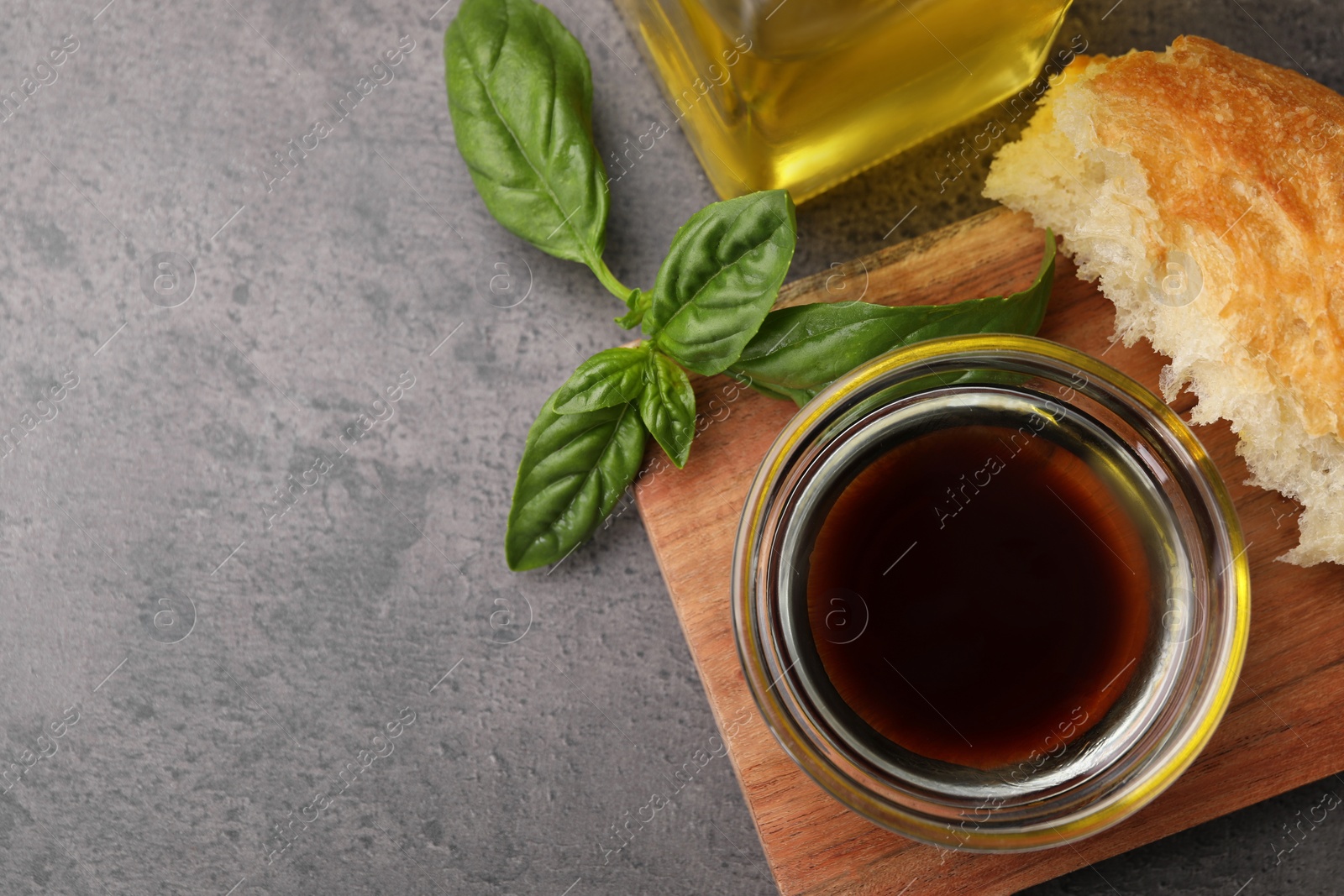 Photo of Bowl of organic balsamic vinegar with oil, basil and bread on grey table, flat lay. Space for text