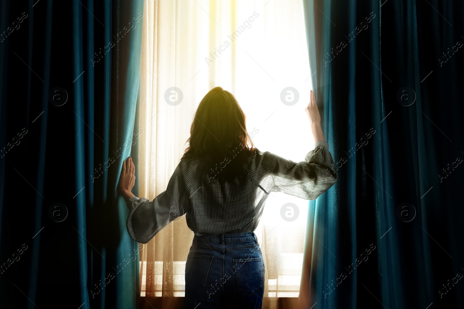 Image of Woman opening window curtains at home, back view