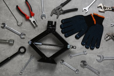 Car scissor jack, gloves and different tools on grey surface, flat lay