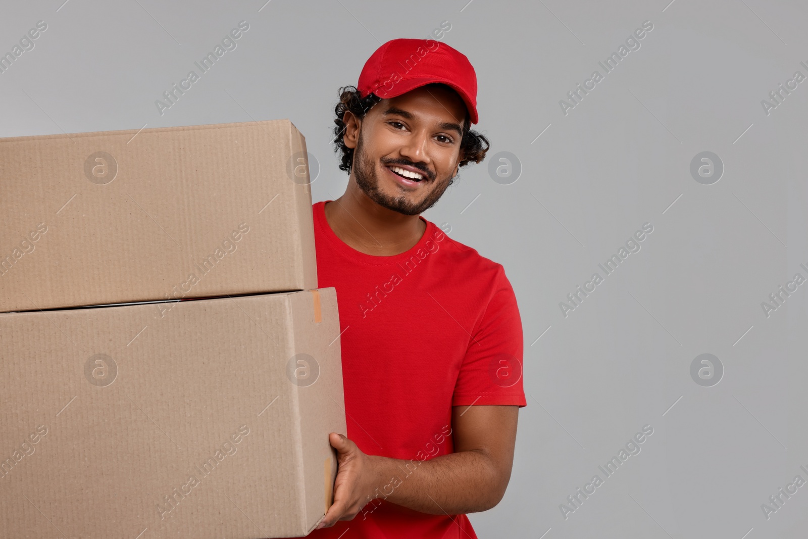 Photo of Happy young courier with parcels on grey background, space for text