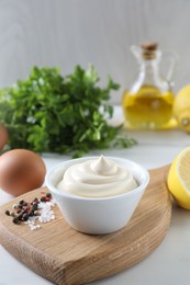 Photo of Tasty mayonnaise sauce in bowl, spices and ingredients on white table