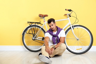 Photo of Handsome young hipster man sitting with bicycle near yellow wall
