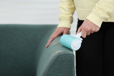 Photo of Woman with lint roller removing pet hair from sofa indoors, closeup. Space for text
