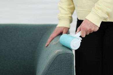 Woman with lint roller removing pet hair from sofa indoors, closeup. Space for text