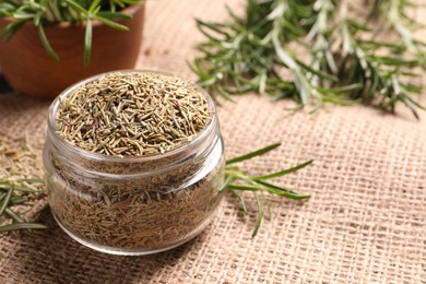 Photo of Jar with dry rosemary on burlap fabric, closeup. Space for text