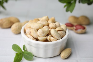 Photo of Fresh peeled peanuts in bowl on white tiled table, closeup