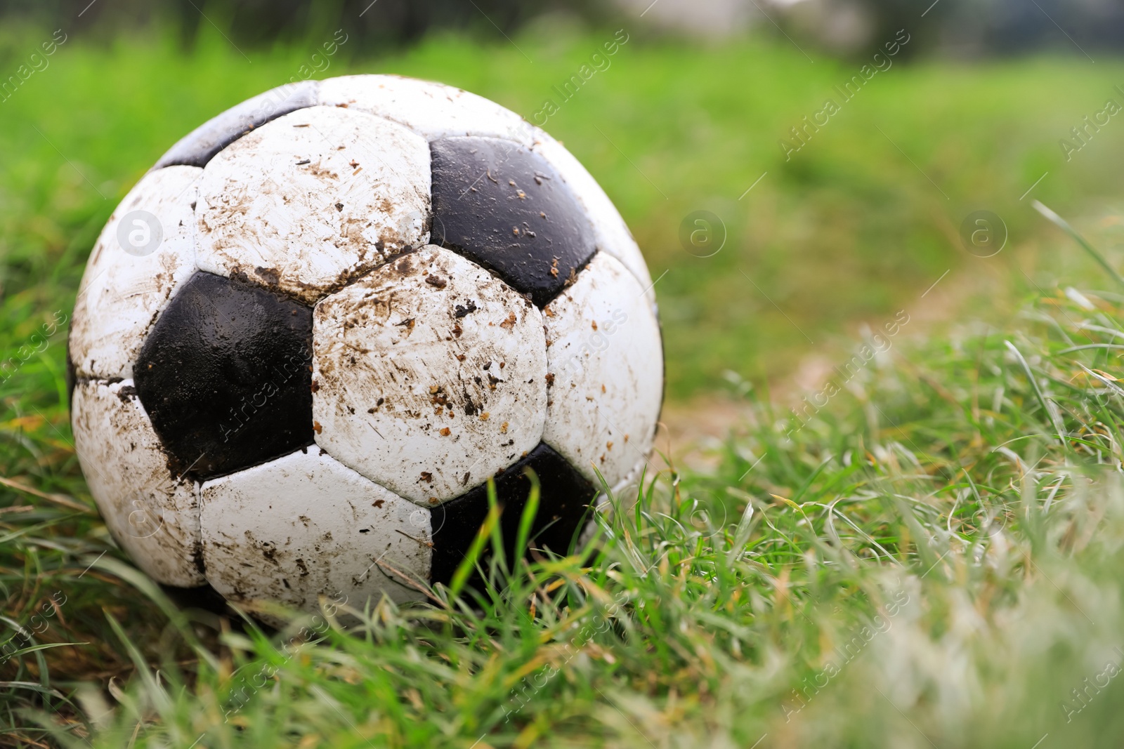 Photo of Dirty soccer ball on green grass outdoors, closeup. Space for text